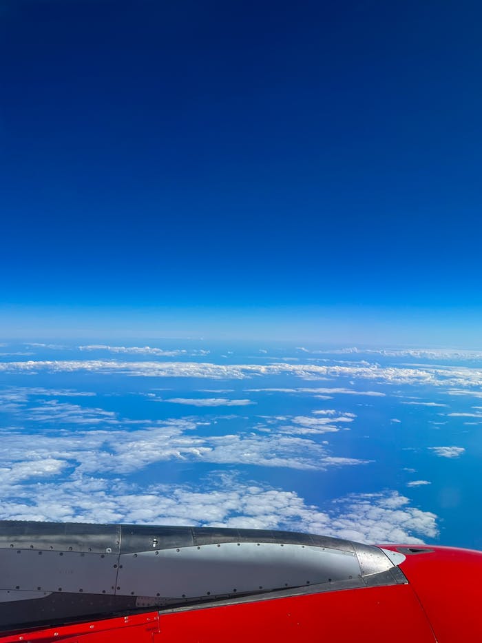 Stunning aerial view of clouds and ocean from airplane window with red wing.